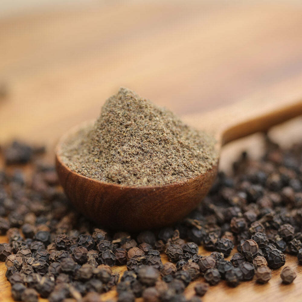 Freshly ground black pepper in a small wooden bowl, surrounded by whole peppercorns