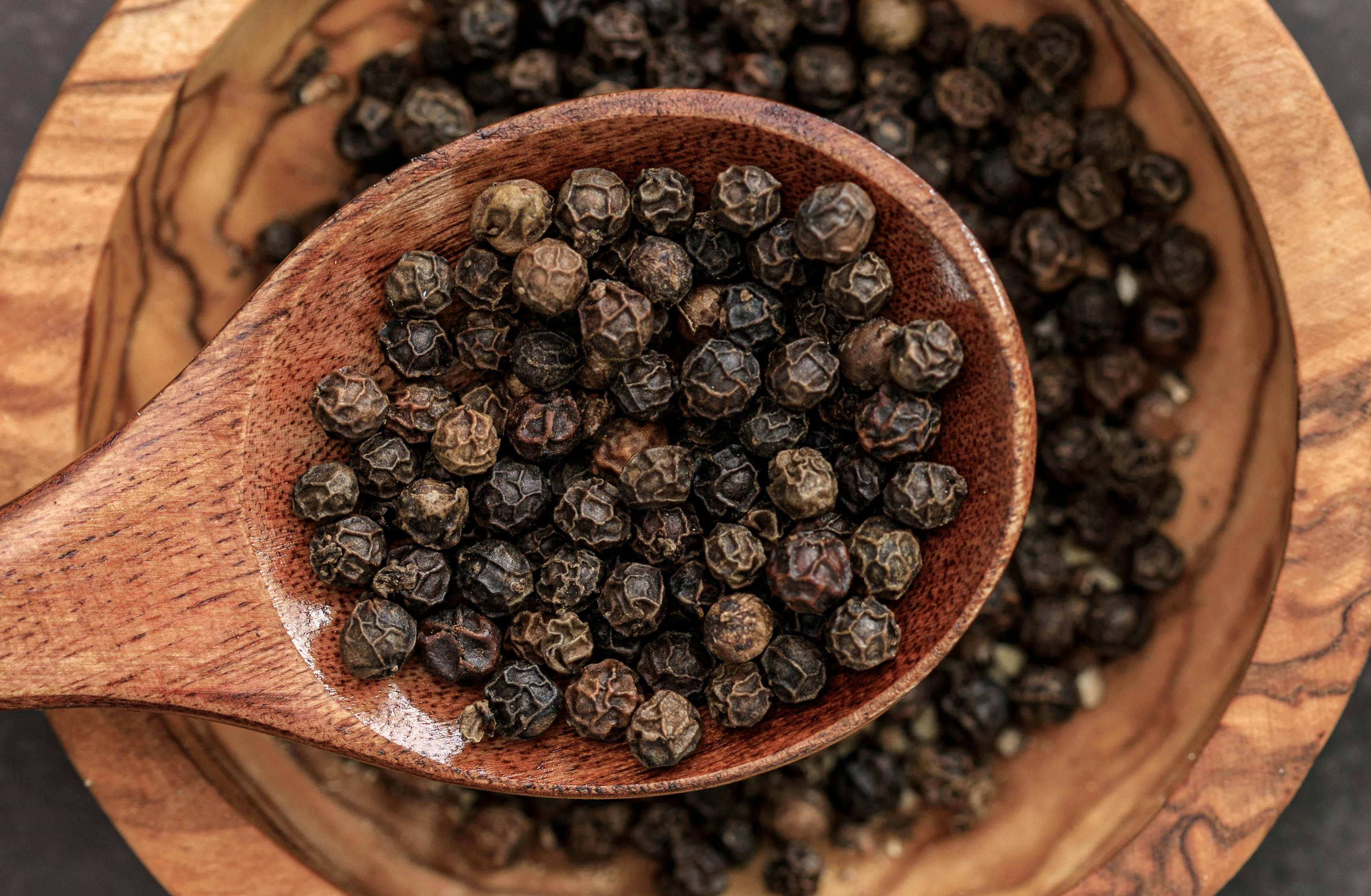 Whole TGSEB Tellicherry peppercorns, freshly cracked in a wooden spoon