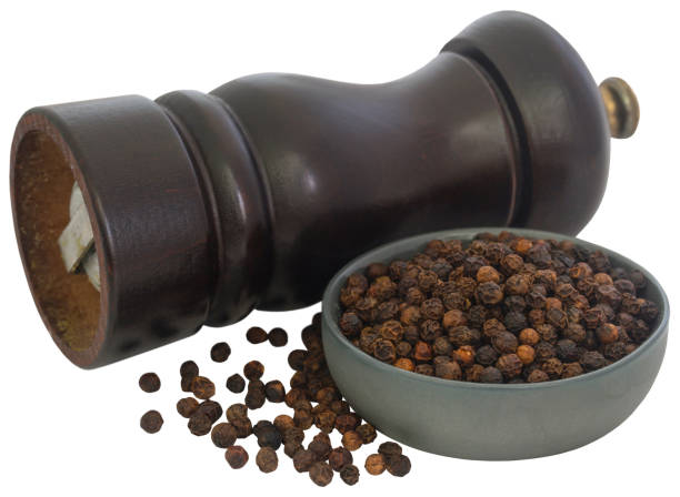 A wooden burr mill pepper grinder beside a bowl of whole black peppercorns